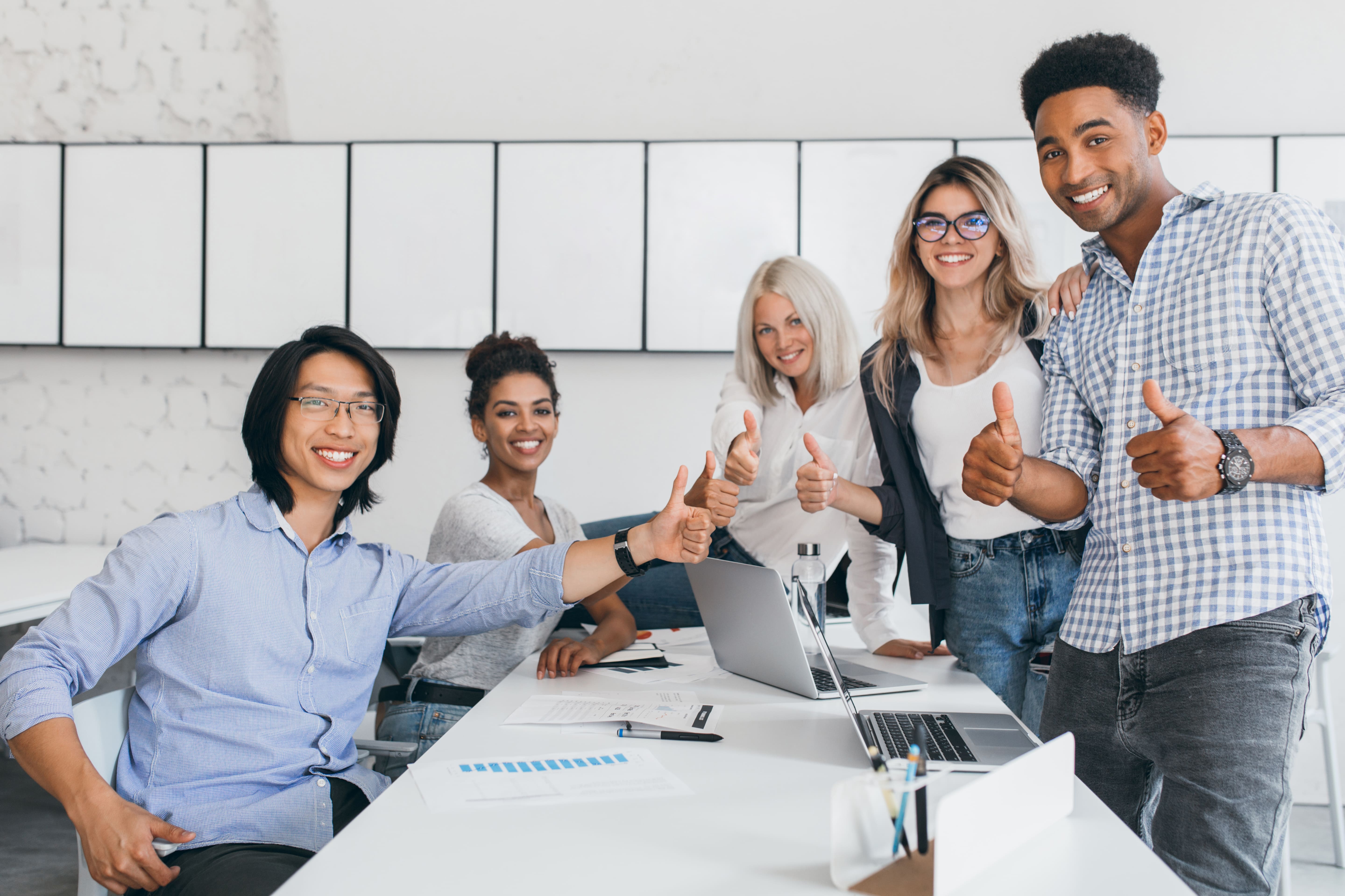 FINAL - blonde-secretary-sitting-table-while-office-workers-posing-with-thumbs-up-indoor-portrait-happy-asian-manager-trendy-shirt-smiling-conference-hall-with-foreign-partners-1